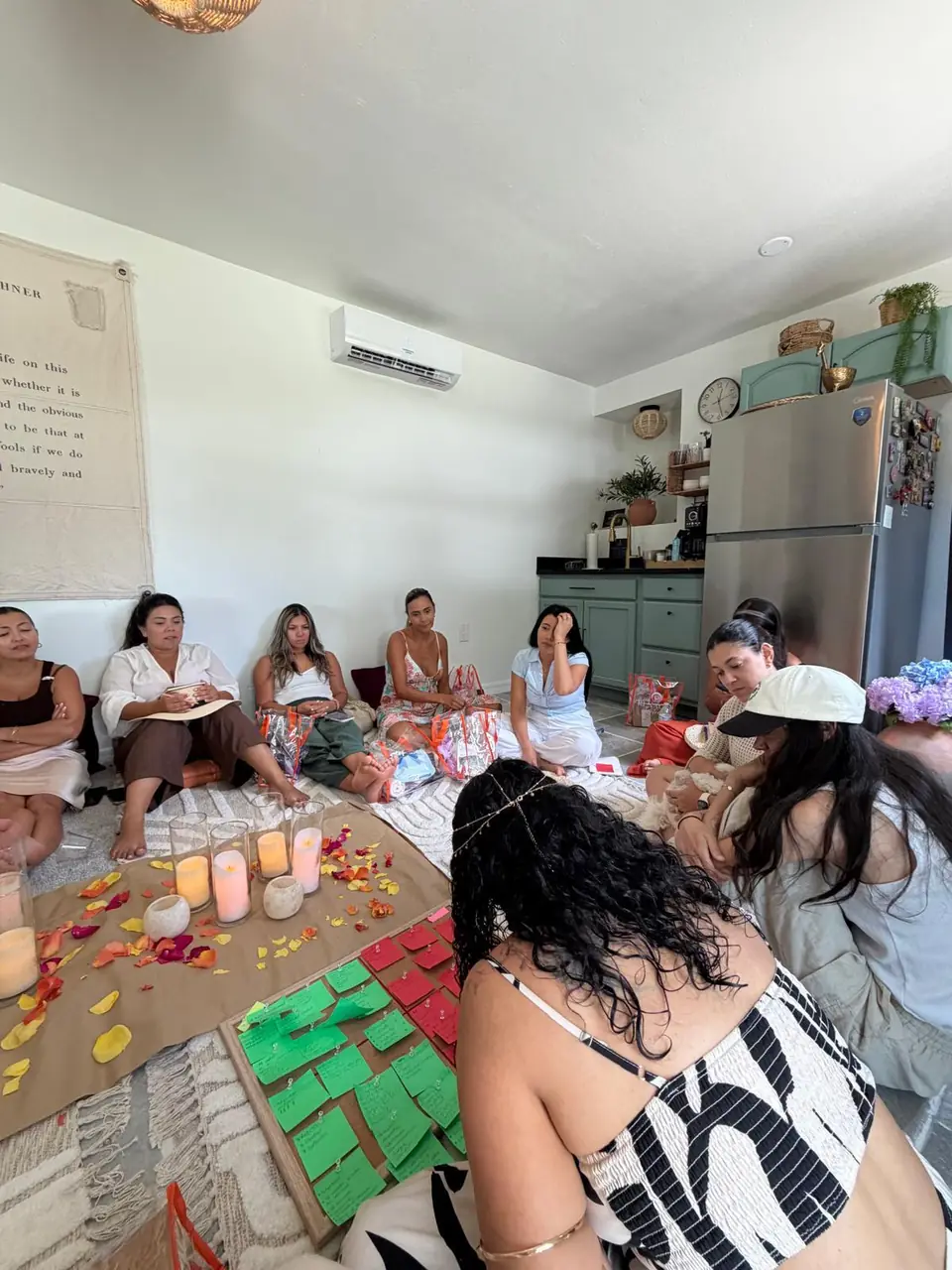 Mujeres sentadas en círculo en una sala, con velas, pétalos de flores y notas de colores en el centro